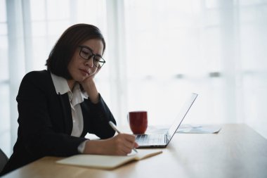 Siluet, ne yazık ki ciddi Asyalı iş kadını stresli depresyonda. Üzücü bir depresyon geçiriyor. Laptop üzerinde çalışıyor ve ofis masasının üzerine not defteri yazıyor. Bunalımlı kadın üzgün ciddi çalışıyor.