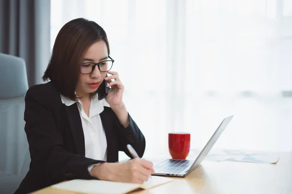 Freelance business woman calling on mobile smartphone while working with laptop, businesswoman mobile phone to calling with customers or shopping online. Smart phone conversation conferrence.