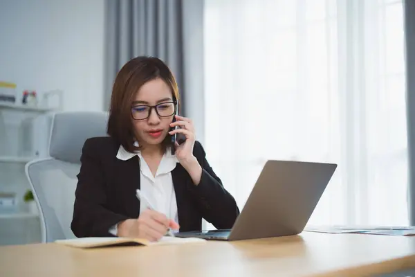 Freelance business woman calling on mobile smartphone while working with laptop, businesswoman mobile phone to calling with customers or shopping online. Smart phone conversation conferrence.