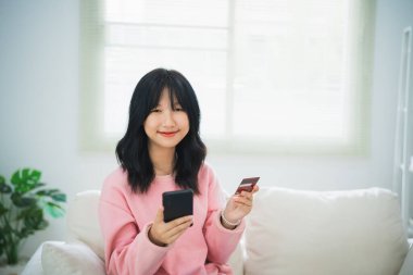 İnternetten alışveriş yapmak için cep telefonu akıllı telefonu kullanan bir kadın. Evde çalışan Asyalı kadın. Çevrimiçi alışveriş, e-ticaret, internet bankacılığı, harcama, ev konseptinden çalışma.