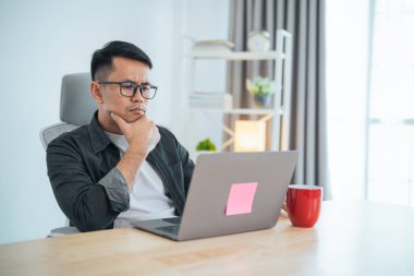 Asyalı iş adamı evde dizüstü bilgisayarla çalışırken stresli depresyon anlarında gözlük takıyor. Depresyondaki adam evde çalışan üzgün adamlar. Herhangi bir yerde çalışma kavramı.