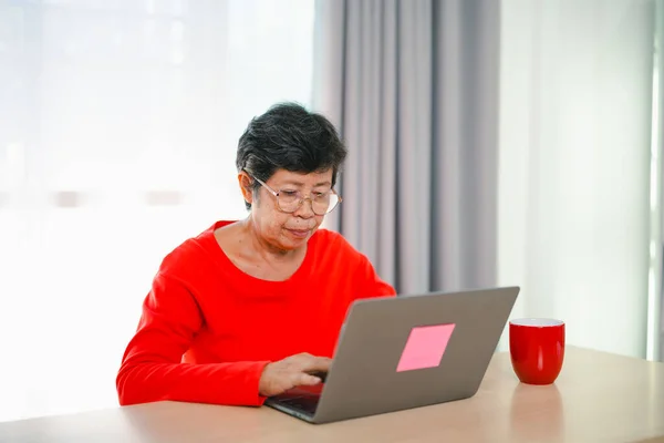 Senior old asian woman working after retirement using laptop at home. Old freelancer working or learning new technology on laptop in living room. Retirement activity concept.