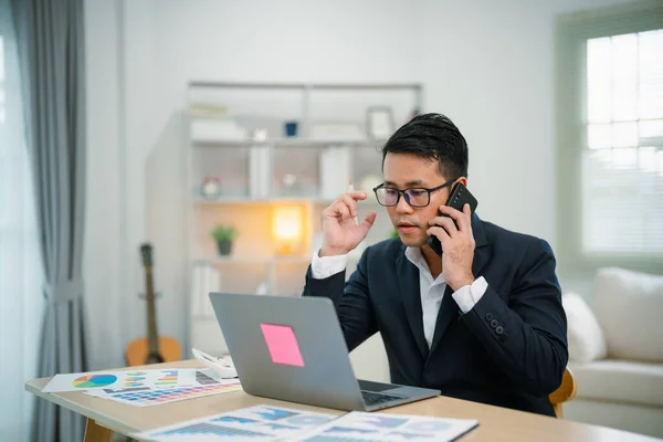 Freelance business man calling on mobile smartphone while working with laptop on table, businessman mobile phone to calling with customers or shopping online. Smart phone conversation conferrence.