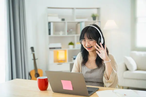Business freelance entrepreneur woman wearing eyeglass and white headphone say hi while conference meeting, working typing keyboard on laptop and on desk table at the home office. Business technology.