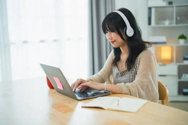Business freelance entrepreneur woman wearing eyeglass and white headphone working typing keyboard on laptop and on desk table at the home office. Business technology concept.