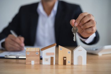Ev kredisi konsepti. Ev modelinin anahtarlarını elinde tutan iş adamı ve müşteri satın alma, sigortalama ve finanse etme sözleşmelerini tartışıyor. Kredi ekonomisi ticari gayrimenkul yatırımları.