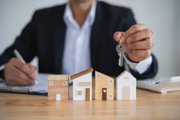 Home loan concept. Business man holding keys house model real estate agent and customer discuss contracts buying, insuring, financing property. Loan finance economy commercial real estate investments.