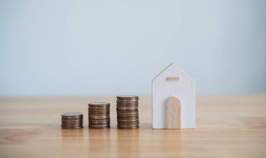 Model ev ve sıra sıra paralar ahşap masaya istiflenir. Plan, emlak satın almak için yatırımları ve tasarrufları finanse eder. Para madeni para ve ev masa başı muhasebe ve vergi ve sigorta kavramına dayanır..