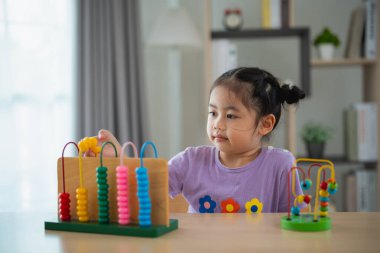 Genç tatlı Asyalı bebek abaküsü renkli boncuklarla öğreniyor. Evdeki oturma odasındaki masada nasıl sayılacağını öğrenmek için. Çocuk bebek gelişimi konsepti çalışıyor.