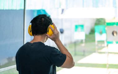 Asyalı tetikçi kulaklık takıyor, kulaklık takıyor ve poligonda kısa atış talimi yapıyor. Meditasyon ve nefsi müdafaa sporları, eğlence aktiviteleri.