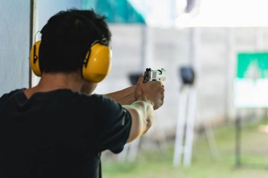 Asyalı tetikçi kulaklık takıyor, kulaklık takıyor ve poligonda kısa atış talimi yapıyor. Meditasyon ve nefsi müdafaa sporları, eğlence aktiviteleri.