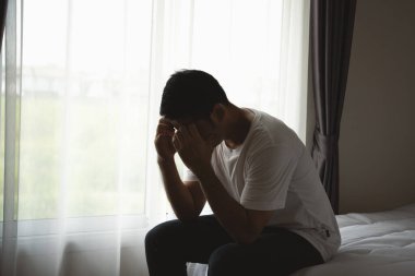 Siluet depresif bir adam yatak odasında yatakta oturuyor. Üzgün Asyalı erkekler uykusuzluk çekiyorlar ve yatak odasında tek başlarına yatıyorlar. Depresyon sağlık insanları kavramı.