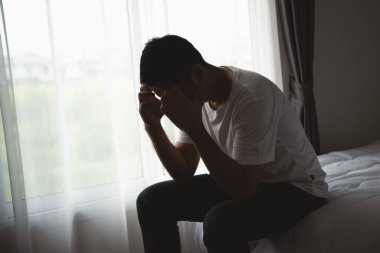 Siluet depresif bir adam yatak odasında yatakta oturuyor. Üzgün Asyalı erkekler uykusuzluk çekiyorlar ve yatak odasında tek başlarına yatıyorlar. Depresyon sağlık insanları kavramı.