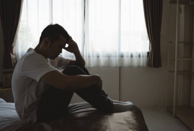 Siluet depresif bir adam yatak odasında yatakta oturuyor. Üzgün Asyalı erkekler uykusuzluk çekiyorlar ve yatak odasında tek başlarına yatıyorlar. Depresyon sağlık insanları kavramı.