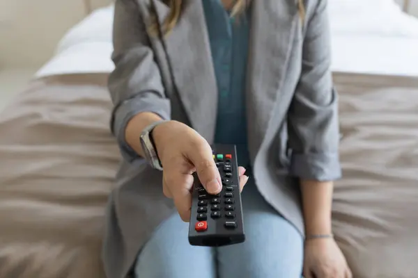 Close up Television remote control in hand woman pointing to tv set and turning it on or off. select channel watching tv at home in the living room relax.