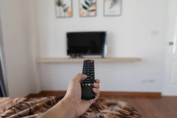Close up Television remote control in hand man pointing to tv set and turning it on or off. select channel watching tv at home in the living room relax.