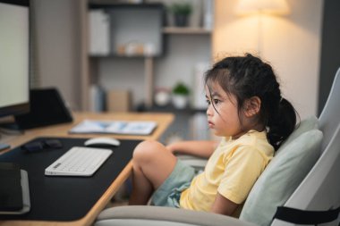 Tişört giyen Asyalı kız bebek dizüstü bilgisayarı kullanmak için konsantre olur ve evdeki oturma odasındaki ahşap masa üzerinde ders çalışır. Eğitim öğrenimi online olarak ev kavramından.