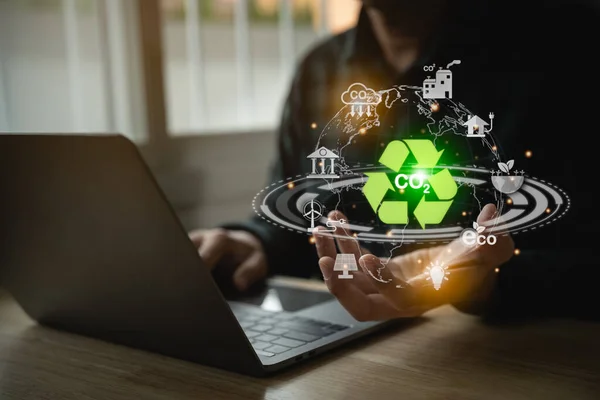 Man holding earth use laptop recycle virtual screen symbol modern reduce CO2 emission with icons, global warming emissions carbon footprint climate. Renewable energy-based green businesses can limit.