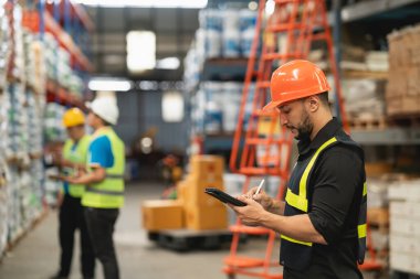Professional manager man employee using tablet check stock working at warehouse. Worker wearing high visibility clothing and a hard hat, helmet and checking and count up goods or boxes for delivery.
