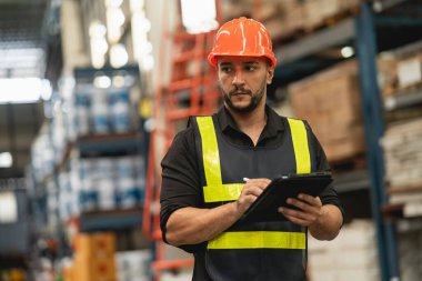Professional manager man employee using tablet check stock working at warehouse. Worker wearing high visibility clothing and a hard hat, helmet and checking and count up goods or boxes for delivery.