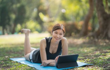 Genç Asyalı kadın yoga egzersizi öğreniyor ya da öğretiyor. Bir video konferansında parktaki yoga minderinde oturuyor. Spor yoga konsepti..