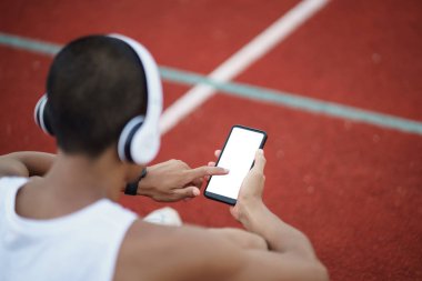 Beyaz kulaklık takan Asyalı sporcu dinlenirken ya da koşuya çıkmadan önce müzik dinlemek için beyaz ekranda cep telefonu kullanıyor ve Lane Stadyumu 'nda egzersiz yapıyor. Spor sağlıklı çalışma konsepti.