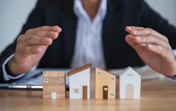 Home loan concept. Business man hand protect house model real estate agent and customer discuss contracts buying, insuring, financing property. Loan finance economy commercial real estate investments.