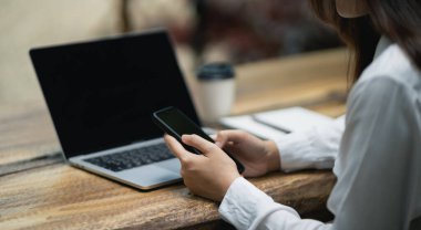 Masada dizüstü bilgisayarla çalıştıktan sonra akıllı telefon kullanan iş kadını, cep telefonu araması yapan ya da sosyal medya kullanan ya da online alışveriş yapan kadın ya da stok ya da kripto para birimi. Akıllı telefon görüşmesi konferansı.