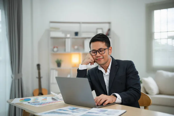 Smart Asian businessman with suit smiling wearing glasses working with computer laptop. concept work form home. Freelance life style, New normal social distancing lifestyle. Work form anywhere concept