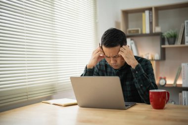 Asyalı serbest çalışan adam dizüstü bilgisayarda video konferansında çalışırken stresli depresyon geçiriyor. Bunalımlı adam evde çalışan üzgün adamlar. Herhangi bir yerde çalış.