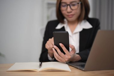 Masada dizüstü bilgisayarla çalıştıktan sonra akıllı telefon kullanan iş kadını, cep telefonu araması yapan ya da sosyal medya kullanan ya da online alışveriş yapan kadın ya da stok ya da kripto para birimi. Akıllı telefon görüşmesi konferansı.