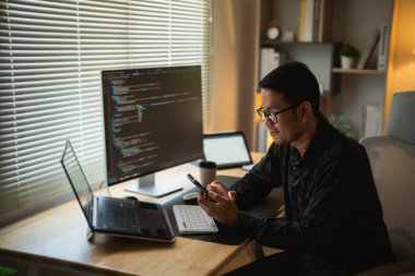 Masada dizüstü bilgisayarla çalıştıktan sonra akıllı telefon kullanan bir adam, iş adamı cep telefonunu arama yapmak veya sosyal medya veya online alışveriş yapmak için kullanıyor. İş konsepti akıllı telefon teknolojisi sohbet konferansı.