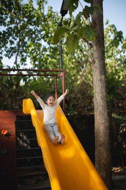 Cute asian girl smile play on school or kindergarten yard or playground. Healthy summer activity for children. Little asian girl climbing outdoors at playground. Child playing on outdoor playground.