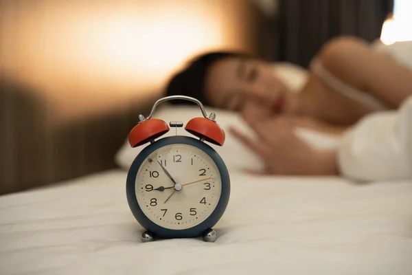 Close up alarm clock. woman sleeping in comfortable bed with silky linens in the morning. Women lying in bed and keeping eyes closed while covered with blanket. cheerful and comfortable.