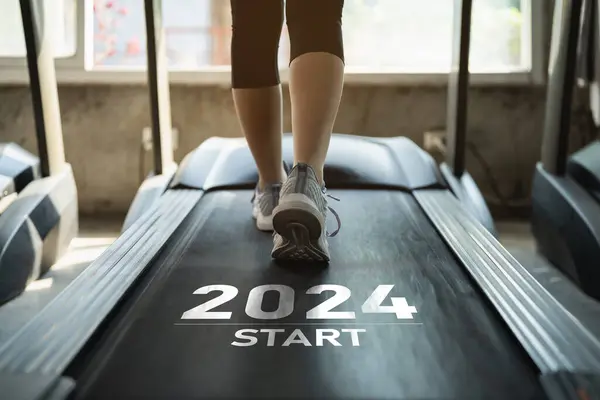 Mutlu yıllar 2024 yeni yılın başlangıcını sembolize ediyor. Ayaklarını kapat, spor kadın koşucu fitness kulübünde koşu bandında koşuyor. Kardiyo çalışması. Sağlıklı yaşam tarzı, spor salonunda erkek eğitimi..