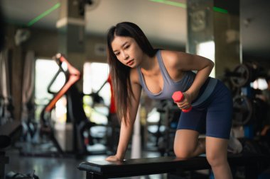 Spor salonunda gülümseyen ve ağırlık egzersizi yapan Asyalı formda bir sporcu. Spor giyimli Asyalı kadın spor salonunda yağ yakmak için egzersiz yapıyor. Spor kadın fitness konsepti.