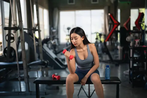 Asian fit sportswoman smiling and working out excercise weights with dumbbells at the fitness gym. asian woman wearing sportwear doing exercise to burn fat at gym. Sport woman fitness concept.