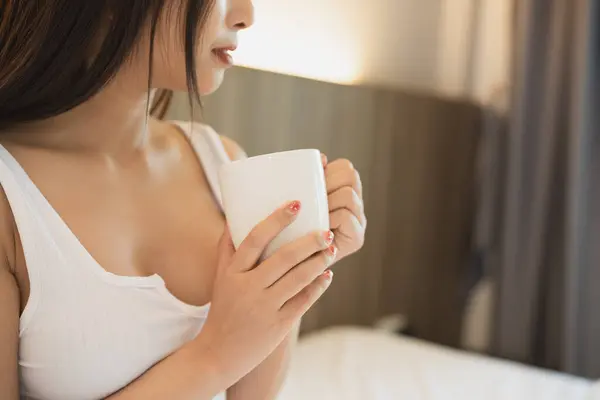 Joyful asian woman drink hot coffee while sitting on the bed in bedroom at home. Asian women relex laying smile after wake up on the bed house. Activity hobby at house concept.