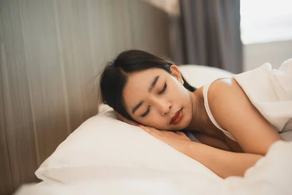 Asian woman sleeping with smart watch showing tracking heartbeat monitor in comfortable bed with silky linens at night light. Women lying in bed and keeping eyes closed while covered with blanket.