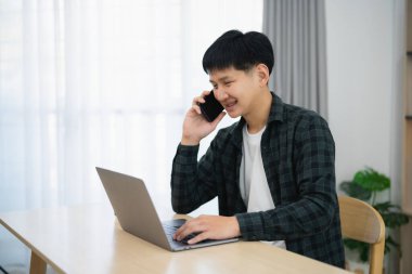 Serbest çalışan bir iş adamı, masada dizüstü bilgisayarla çalışırken cep telefonundan arıyor, müşterilerle görüşmek için iş adamı cep telefonu kullanıyor ya da internetten alışveriş yapıyor. Akıllı telefon görüşmesi konferansı.