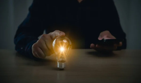 Businessman holding bright light bulb and using mobile phone. Concept of Ideas for presenting new ideas Great inspiration and innovation new beginning.Innovation through ideas and inspiration ideas.