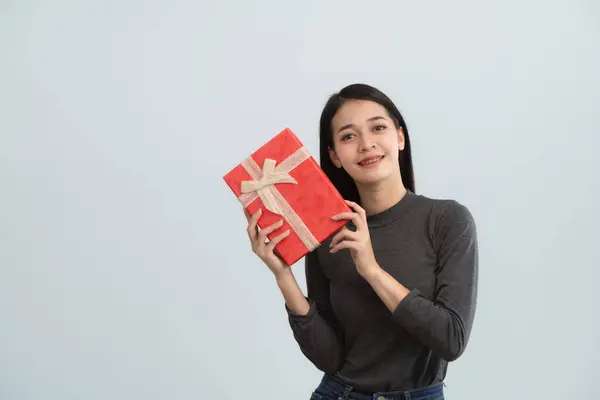Asian woman with braces smiling happy and hold in hand present box with gift ribbon bow look aside isolated on grey background studio. Lifestyle concept.