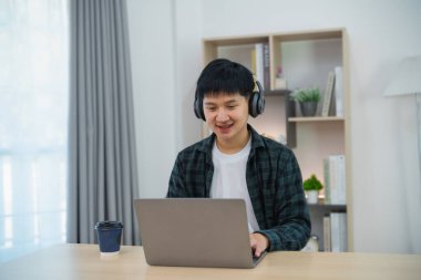 Bilgisayar laptopuyla çalışan, gülümseyen diş telleri olan kulaklık takan zeki bir Asyalı. Evdeki iş formu. Serbest yaşam tarzı, yeni normal sosyal mesafeli yaşam tarzı. Çalışma formu herhangi bir konsept.