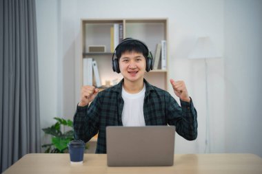 Telli, gülümseyen akıllı Asyalı adam bilgisayar laptopuyla çalışırken neşeli bir şekilde elini kaldırdı. Evdeki iş formu. Yeni normal sosyal mesafeli yaşam tarzı. Çalışma formu herhangi bir konsept.