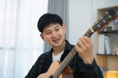 Asyalı adam youtuber canlı yayında gitar çalıyor ve şarkı söylüyor. Asyalı adam gitar öğretiyor ve internette şarkı söylüyor. Dizüstü bilgisayarlı ve akustik gitar çalan müzisyen müziği.