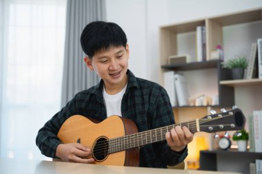 Asyalı adam youtuber canlı yayında gitar çalıyor ve şarkı söylüyor. Asyalı adam gitar öğretiyor ve internette şarkı söylüyor. Dizüstü bilgisayarlı ve akustik gitar çalan müzisyen müziği.