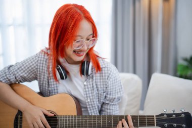 Evdeki oturma odasında kanepede otururken gitar çalan gözlüklü ve kulaklık takan Asyalı bir kadın. Evde gitar çalarken şarkı yazan Asyalı kadınlar. Şarkı müziği konsepti oluştur.