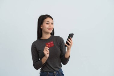 Kredi kartı ve cep telefonunu internetten alışveriş için gösteren Asyalı bir kadın beyaz ya da gri arka plan stüdyosunda izole edilmiş. Çevrimiçi alışveriş, e-ticaret, internet bankacılığı, para harcama kavramı.