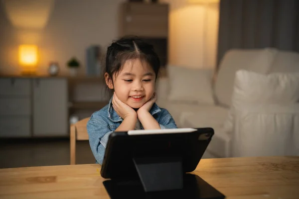 Asian child girl looking using and touch tablet display screen. Baby smiling funny time to use tablet. Too much screen time. Cute girl watching videos while tv, Internet addiction concept.