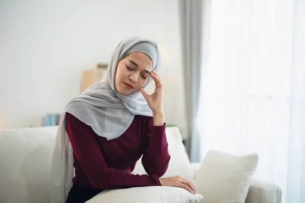 Muslim islam Asian woman wearing hijab depressed sadly serious  having stressful depression sad time sitting on sofa in the living room at home. Depression woman sad serios health mental concept.
